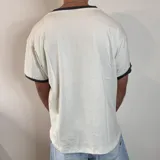 Remera de corte regular color blanco con detalles en gris oscuro en el cuello y los bordes de las mangas. Presenta un estampado pequeño centrado en el pecho.