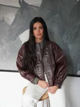 Campera de cuero color camel, de silueta oversize y levemente corta. Cuenta con cierre frontal metálico, cuello redondo a la base y mangas amplias. Presenta detalles de costuras trenzadas en el frente.