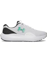 Championes de running Under Armour modelo Charged Surge 4, color blanco con detalles en negro y logo en verde agua. Presentan parte superior de malla transpirable con superposiciones sintéticas, plantilla Deluxe Comfort System y entresuela Charged Cushioning para mayor amortiguación y respuesta.