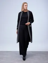 Cardigan largo tejido de punto color negro con detalles de líneas blancas en los bordes delanteros, puños y bolsillos. Cuenta con mangas largas y bolsillos frontales aplicados con botones decorativos dorados.