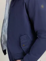 Campera Harrington color beige, con cuello alto abotonado, cierre frontal completo y bolsillos laterales con solapa y botones a presión. Puños y cintura elastizados de rib.