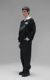 Sweater de punto negro con cuello polo en color crema, manga larga y diseño oversize. Presenta bordados en el frente con la inscripción 'Ravers', el número '90' y letras cursivas, con terminaciones en punto rib en puños y cuello.