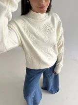 Sweater de punto color blanco con cuello polera, manga larga y diseño bordado al tono con motivos florales en el frente y las mangas.