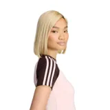 Remera Adidas SST de color rosado claro, con cuello redondo y mangas cortas en color marrón oscuro que presentan las tres tiras características de la marca en tono claro. Incluye el logo del trébol bordado en el pecho.