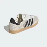 Championes Adidas Samba OG con diseño de malla transpirable y detalles en cuero. Presenta las icónicas tres bandas laterales en negro, puntera reforzada y suela de goma color caramelo.