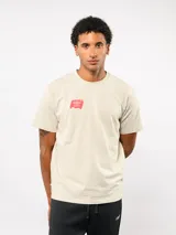 Remera de manga corta color beige, con cuello redondo y logo de Umbro estampado en color rojo en el pecho.