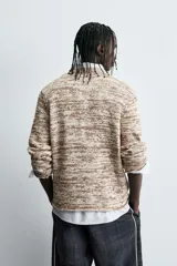 Jersey de punto con cuello redondo y manga larga, confeccionado en mezcla de algodón con textura jaspeada en tonos beige y marrón.