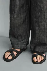 Sandalia plana negra con tiras anchas cruzadas sobre el empeine y una tira que separa el dedo gordo. Posee plantilla anatómica.