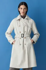 Trench impermeable color beige de corte clásico, con cierre frontal de doble botonadura, solapas amplias y cinturón ajustable con hebilla. Incluye capucha desmontable y bolsillos laterales.