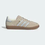 Championes Adidas Gazelle Indoor de gamuza color beige con las icónicas tres tiras en celeste claro. Presenta suela de caucho traslúcido y detalles en dorado.