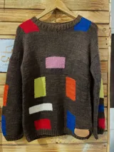 Sweater tejido a mano de lana merino 100%, color marrón con diseño geométrico multicolor y detalles artesanales. Presenta cuello redondo, mangas largas y corte holgado.