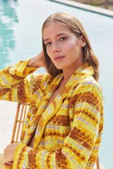 Saco largo de tejido de punto con diseño geométrico multicolor en tonos amarillo, marrón y lila. Presenta una abertura frontal con solapas, bolsillos delanteros y un cinto para ajustar en la cintura.