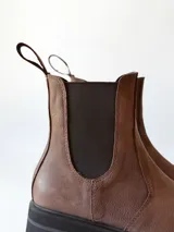 Bota tipo Chelsea de cuero color chocolate, con paneles elásticos laterales, tirador trasero y suela track negra de goma.