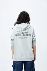 Canguro negro con capucha y bolsillo delantero. Presenta un bordado frontal y trasero con lettering “Mont Saint-Michel”.