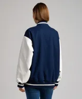 Campera bomber azul marino con mangas blancas, cuello, puños y ruedo acanalados con rayas blancas y azul marino. Tiene cierre frontal con botones a presión y un pequeño bordado en el pecho.