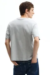 Remera de algodón gris jaspeado con cuello redondo y mangas cortas. Presenta un estampado frontal con la inscripción 'NEWPORT' en tipografía universitaria verde oscuro y 'RHODE ISLAND' debajo.