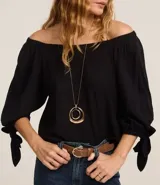 Blusa negra de viscosa con escote off-shoulder, mangas 3/4 con elásticos y lazos en los puños.