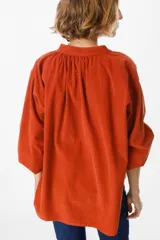 Camisa de pana color verde oliva, con cuello mao, cierre frontal de botones y mangas largas abullonadas con puños elásticos.