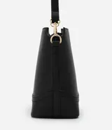 Cartera tipo hobo de tamaño pequeño, confeccionada en material sintético color marrón oscuro con acabado liso. Presenta una correa ajustable, cierre principal con cremallera y detalles metálicos dorados, incluyendo una placa con el logo de la marca en el frente.