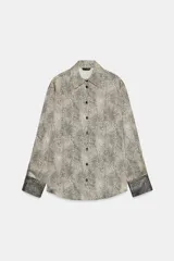 Camisa de manga larga con cuello solapa y cierre frontal de botones. Presenta un estampado de puntos pequeños en tono crema y negro, con puños en contraste que incluyen un estampado más denso.