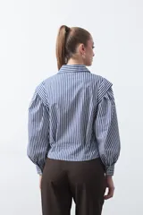 Camisa a rayas azules y blancas de manga larga, con cuello clásico y puños abotonados. Presenta un diseño entallado en la cintura.