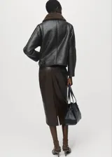 Chaqueta efecto piel de color negro con diseño oversize, cuello camisero y forro interior de borreguito marrón. Cuenta con cierre frontal de cremallera, manga larga y dos bolsillos de parche laterales.