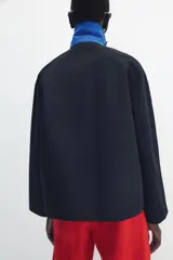 Chaqueta de Zara Woman Collection color negro, de cuello con solapa y manga larga. Cuenta con bolsillos delanteros ocultos en las costuras, cierre frontal con botones metálicos a presión y detalle de diseño asimétrico en azul en el cuello.