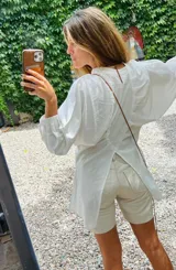 Camisa de lino blanca, de corte oversize, con mangas largas abullonadas, cuello mao y botones. Es más larga en la parte trasera e incluye un tajo en la espalda.