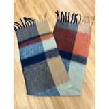 Bufanda rectangular de tejido grueso con diseño de cuadros en tonos azul, naranja, gris y beige, terminada con flecos en los extremos.