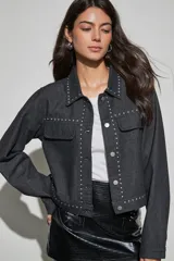 Campera de denim color negro con detalles de tachas metálicas en cuello, solapas, solapa de cierre y bolsillos frontales. Posee cierre frontal con botones metálicos y bolsillos con solapa en el pecho.