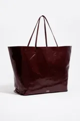 Bolso shopper grande Bimba Y Lola confeccionado en cuero vacuno con acabado brillante en color bordó. Cuenta con estructura blanda, doble asa fina de hombro y detalle de logo metálico en la parte inferior.