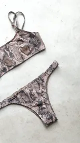 Conjunto de bikini con corpiño estilo bandó alto y breteles regulables, con lazo para atar en la espalda. La bombacha es vedetina con frunce elástico en los costados. Presenta un estampado tipo tie-dye o marmolado en tonos azules y naranjas/terracota.