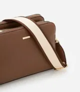 Bolso bandolera de tamaño mediano confeccionado en poliuretano color marrón. Presenta tres compartimentos independientes con cierre de cremallera, herrajes metálicos dorados y una correa de hombro ajustable de cinta tejida bicolor.