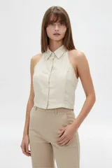 Top halter color beige, confeccionado en viscosa, de corte al cuerpo y sin mangas, con cierre frontal de botones y detalles de costuras decorativas.