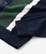 Cardigan masculino de punto con cuello camisero y cierre frontal de botones. Presenta un diseño con paneles frontales en color verde y blanco que contrastan con el cuerpo azul marino, destacando por su textura de tejido diferenciada.