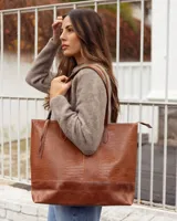 Bolso tipo tote de cuero vacuno, color marrón, con textura efecto reptil en la parte superior y base de cuero liso. Cuenta con doble asa de hombro y cierre superior.