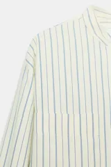 Camisa de corte oversize confeccionada en tejido con viscosa, con estampado de rayas verticales. Presenta cuello mao, cierre frontal con botones ocultos bajo solapa, mangas largas con puños anchos y bolsillos de plastrón en el delantero. El bajo es asimétrico y redondeado.
