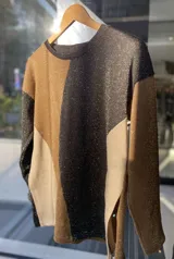 Buzo de tejido fino combinado en colores beige, negro y natural, con cuello redondo y mangas largas.