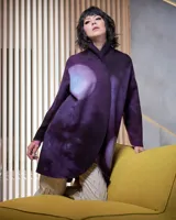 Tapado de lana merino afieltrada color violeta con teñido artesanal Tie Dye en forma de luna. Tiene cierre cruzado asimétrico con broches, cuello alto y bolsillos laterales.