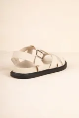 Sandalia baja de tiras cruzadas color camel, con hebilla metálica ajustable en el tobillo y suela negra gruesa.