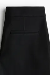 Pantalón sastrero negro de corte acampanado, con cierre, botón oculto y corchetes. Incluye bolsillos al bies y bolsillos traseros ribeteados, con pliegues en la parte delantera y trasera de las piernas.