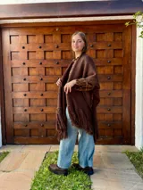 Ruana tejida en color chocolate, confeccionada en lana, con diseño de textura lisa y terminaciones con flecos largos en los extremos.