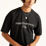 Remera negra de algodón New Balance modelo Trackside, con cuello redondo acanalado, mangas cortas y calce cuadrado. Presenta estampado gráfico en relieve con la marca en el centro del pecho.