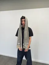 Bufanda larga de tejido trenzado con diseño de cuadros en tonos beige, marrón, negro y blanco. Presenta flecos en los extremos, una grifa de goma con logo en una punta y una etiqueta tejida con logo en la otra.