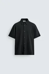 Camisa regular fit negra de manga corta, con cuello bowling y cierre frontal de botonadura. Confeccionada en tejido texturizado con elasticidad y aberturas laterales en el bajo.