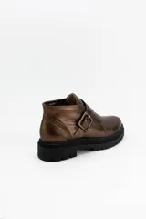 Botines de cuero metalizado en tono oscuro con acabado brillante. Presentan un diseño de corte bajo con una hebilla lateral decorativa y suela de goma negra con plataforma dentada.