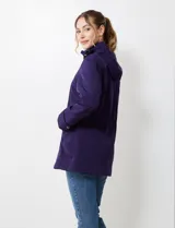 Gabardina impermeable de mujer, color morado oscuro, con capucha desmontable y cierre frontal oculto con botones a presión. Presenta bolsillos delanteros y ajuste interno en la cintura.