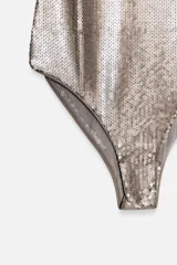 Body de escote en pico con tirantes finos, completamente cubierto de lentejuelas brillantes. Cuenta con cierre en el bajo mediante botones a presión.