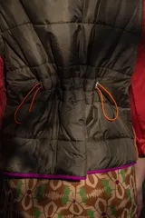 Chaleco puffer con estampado abstracto en tonos marrones, verdes y fucsia. Tiene cuello alto, cierre frontal con cremallera y ribete fucsia.