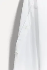 Camisa blanca de algodón con cuello solapa, manga larga con puños abotonados, cierre frontal con botones y detalle de tejido combinado en el frente.